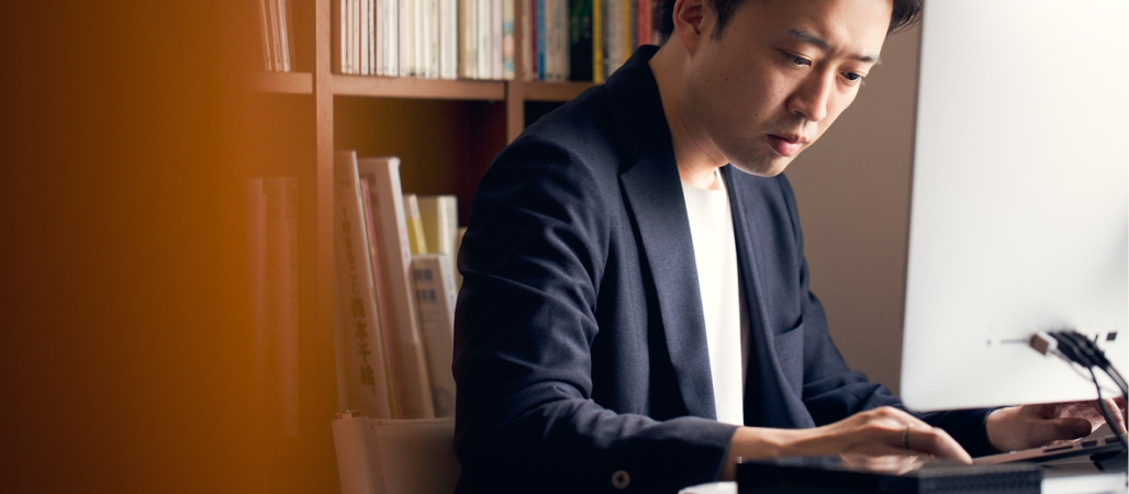Image of man sitting in an office space while typing on a keyboard with a monitor in front.