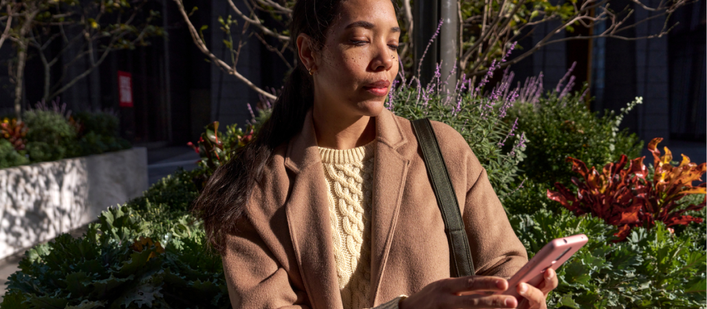 Image of a woman sitting down outside looking at her phone.