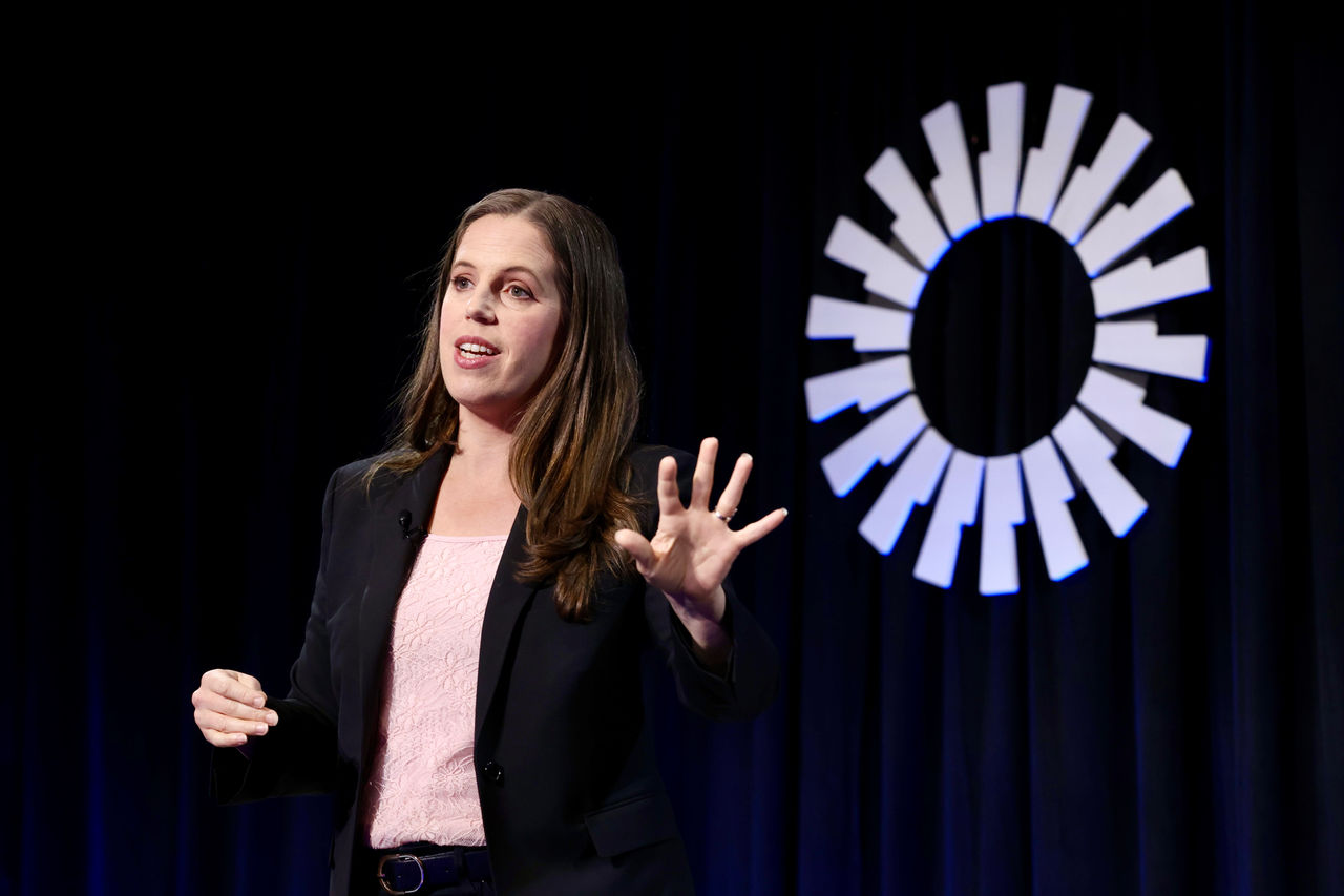 Sabrina Lea in a black blazer and pink top speaking on stage.