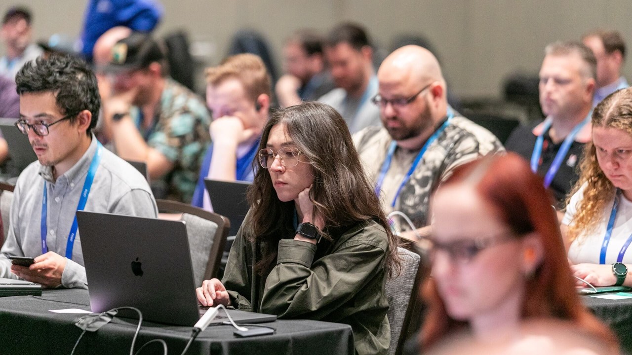A group of Oktane attendees in a conference session, focused on their laptops.