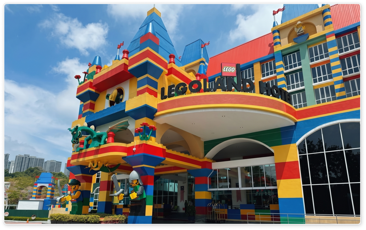 A brightly colored Lego-themed hotel exterior is shown under a blue sky with scattered clouds. 